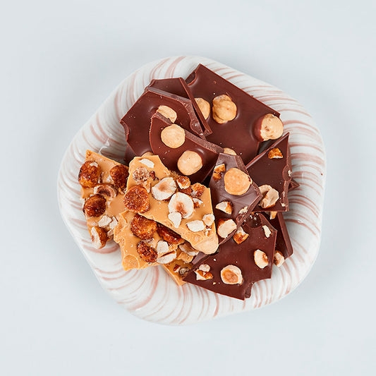 Stykker af Summerbird Amber og mørk chokolade med hele hasselnødder på en lille tallerken.