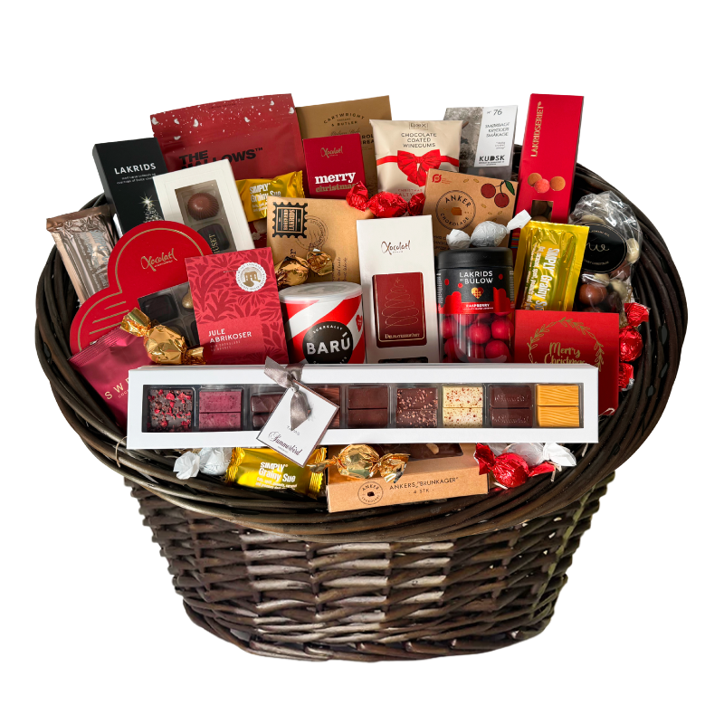 Stor luksuskurv fyldt med chokolade, lakrids og håndplukkede delikatesser, smukt præsenteret i en fletkurv indpakket i cellofan og pyntet med gavebånd
