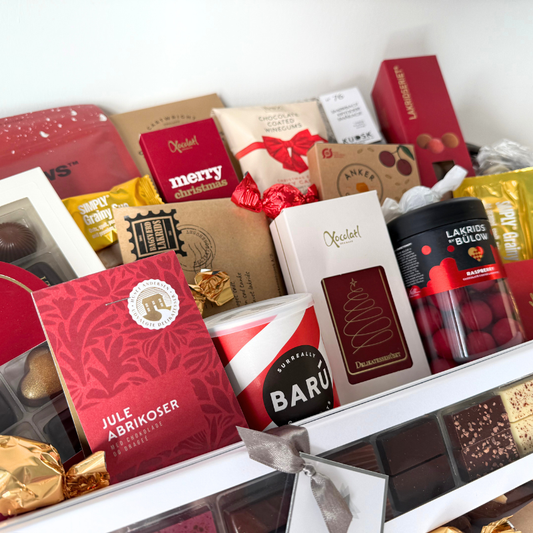 Stor luksuskurv fyldt med chokolade, lakrids og håndplukkede delikatesser, smukt præsenteret i en fletkurv indpakket i cellofan og pyntet med gavebånd