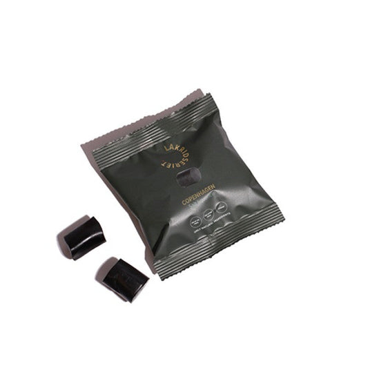 Grøn pose med saltlakrids fra Lakridseriet og to sorte lakridsstykker på hvid baggrund.